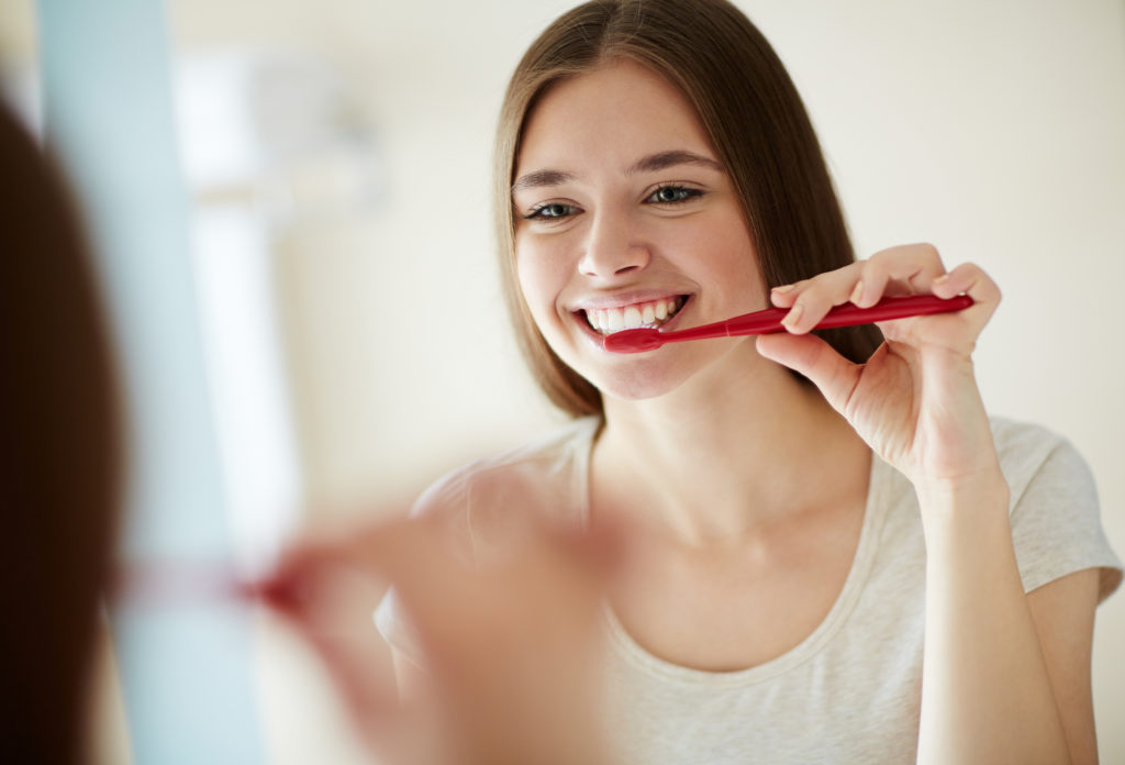 Young girl looks in the mirror as she brushes her teeth