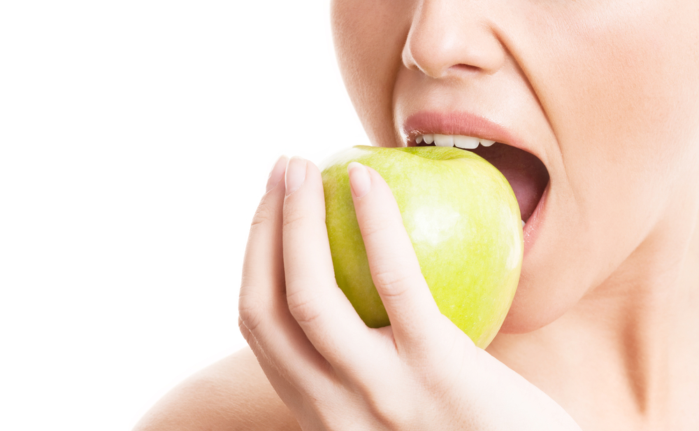 A young girl takes a bite into a green apple