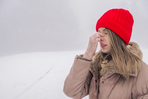 Girl in coat and red ski cap has headache in snowy outdoors