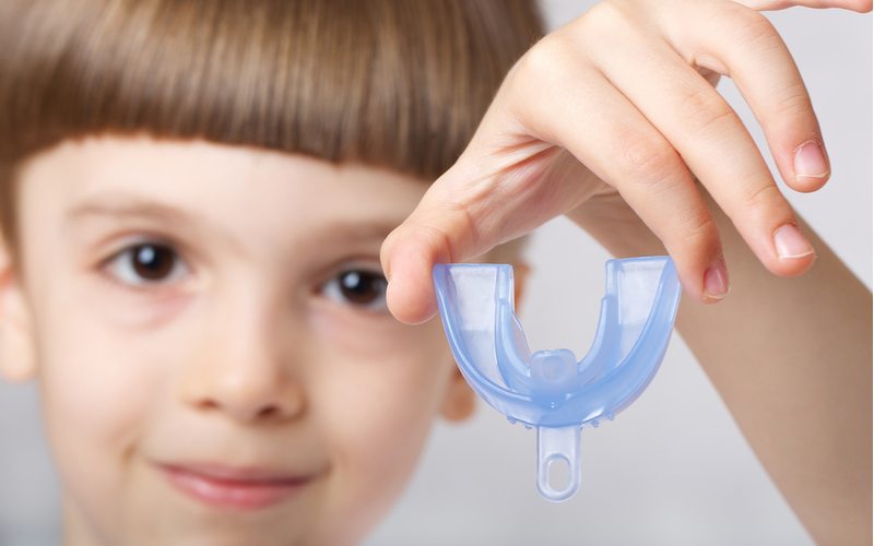 A small boy holds up a dental mouthguard